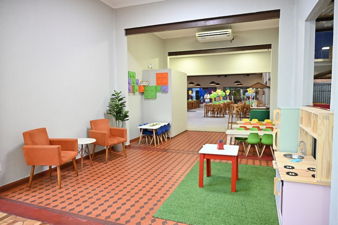 Área infantil com casinha de brinquedo, mesinhas e tapete verde