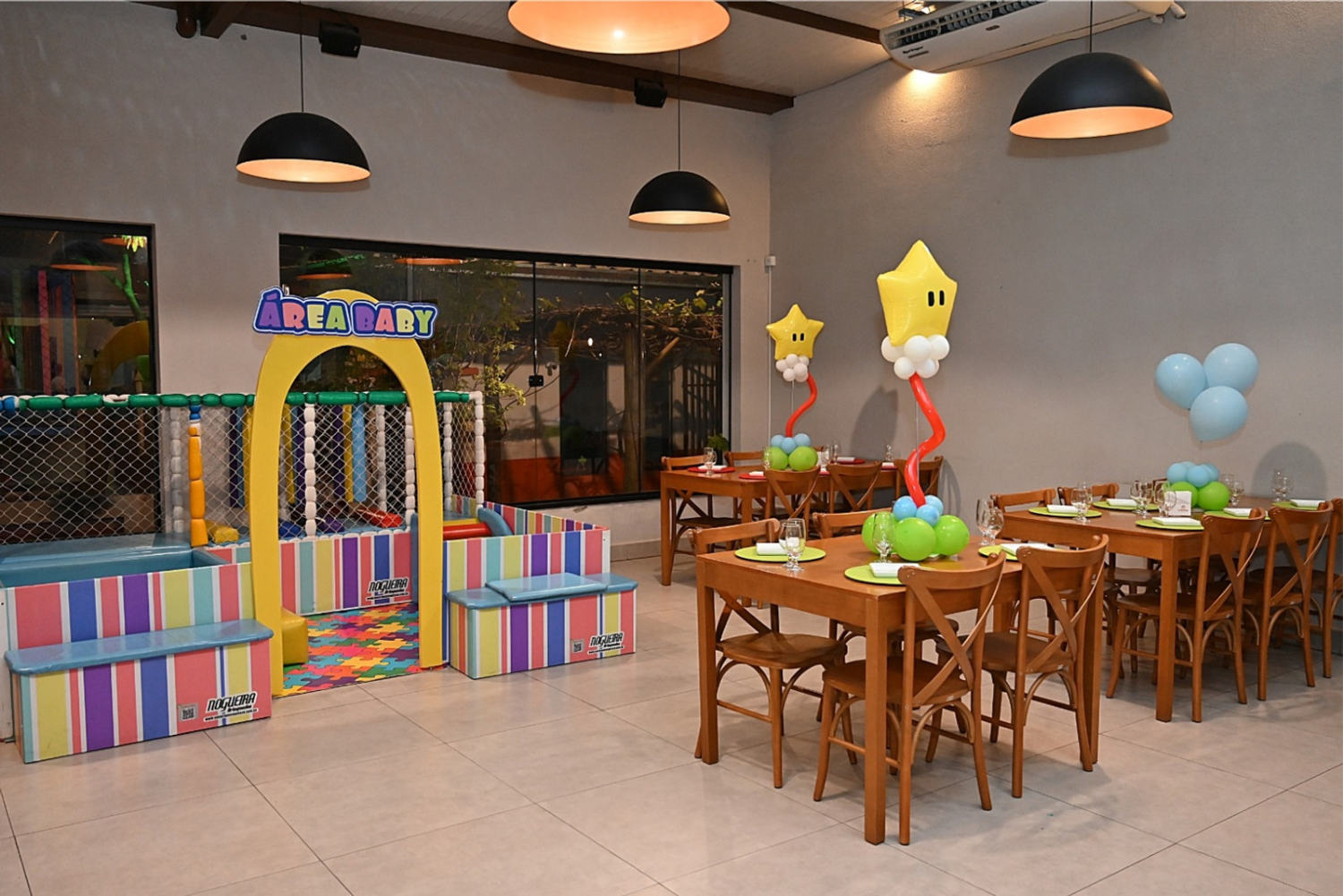 Salão principal do Espaço Carrossel, com mesas de madeira, área baby e brinquedão ao fundo
